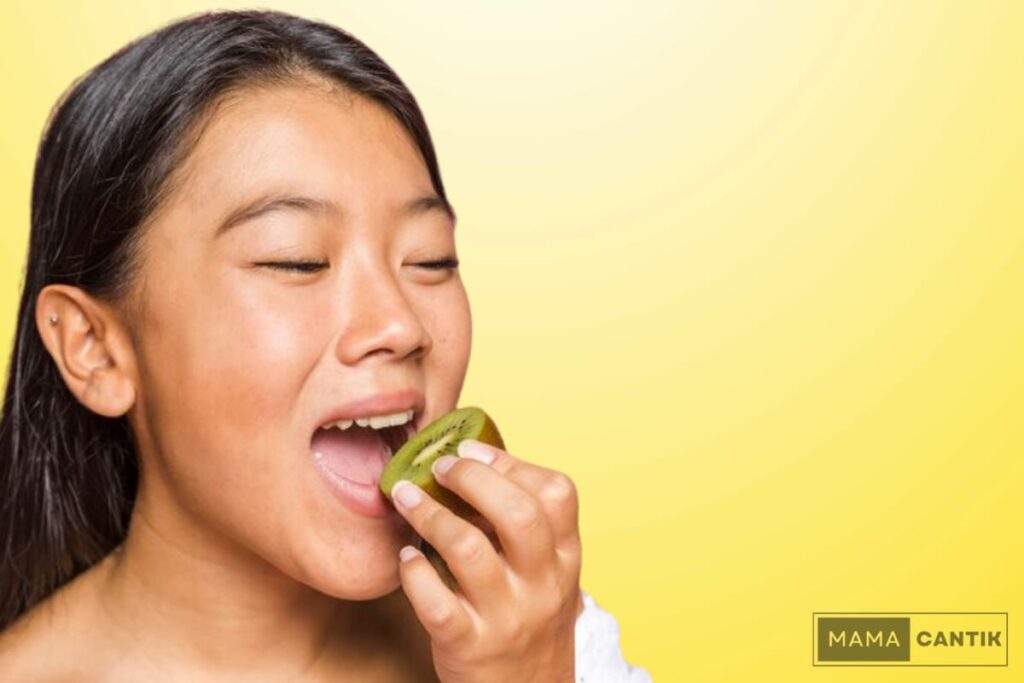 Seorang wanita sedang menikmati potongan buah kiwi