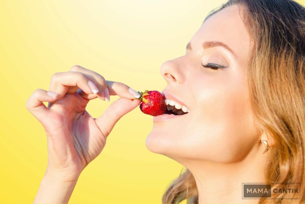 Wanita sedang makan buah stroberi